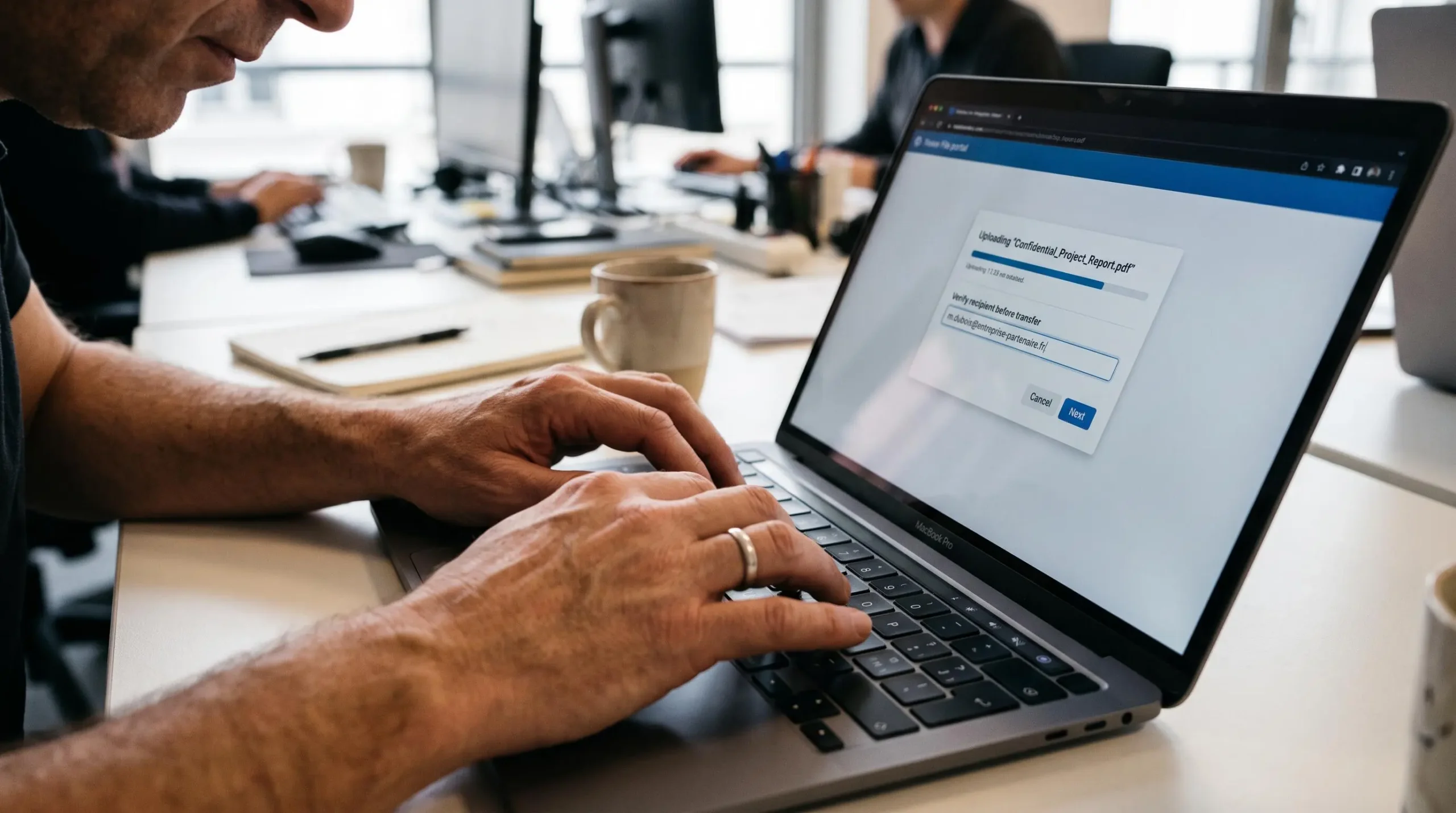Gros plan sur des mains saisissant un destinataire dans une plateforme sécurisée de partage de fichiers sur un ordinateur portable.